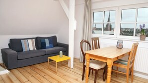 A modern living room with a grey sofa, a yellow coffee table, and a wooden dining table with chairs. - Studio with a panoramic view, centrally located in the Old Town, quiet, Wi-Fi, free parking (FL)