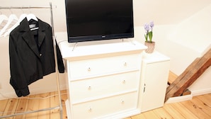 A white dresser with a flat-screen TV on top, a coat rack with a black jacket, and a potted plant with purple flowers. - Studio with a panoramic view, centrally located in the Old Town, quiet, Wi-Fi, free parking (FL)