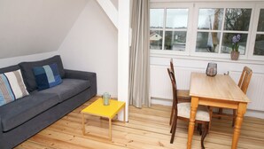 Una sala de estar con un sofá gris, una mesa de centro amarilla y una mesa de comedor de madera con sillas.