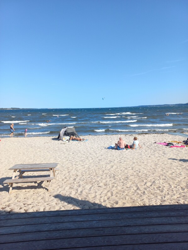 Une plage de sable avec un banc en bois, une tente et des personnes qui se détendent.