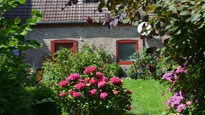 Ett hus byggt av tegel med ett tak täckt av takpannor, två fönster med röda ramar och en trädgård med rosa blommor.
