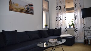 Ett modernt vardagsrum med en soffa i mörk färg, ett soffbord i glas och en platt-TV som är monterad på väggen.