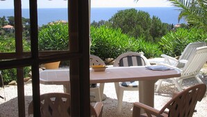 An outdoor seating area with a table and chairs, overlooking a scenic view of the sea and greenery. - Typical house of Provence in quiet surroundings, with breathtaking sea-view (Le Lavandou)