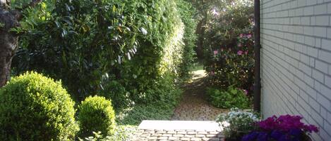 A garden pathway with a brick surface leading to a white building.