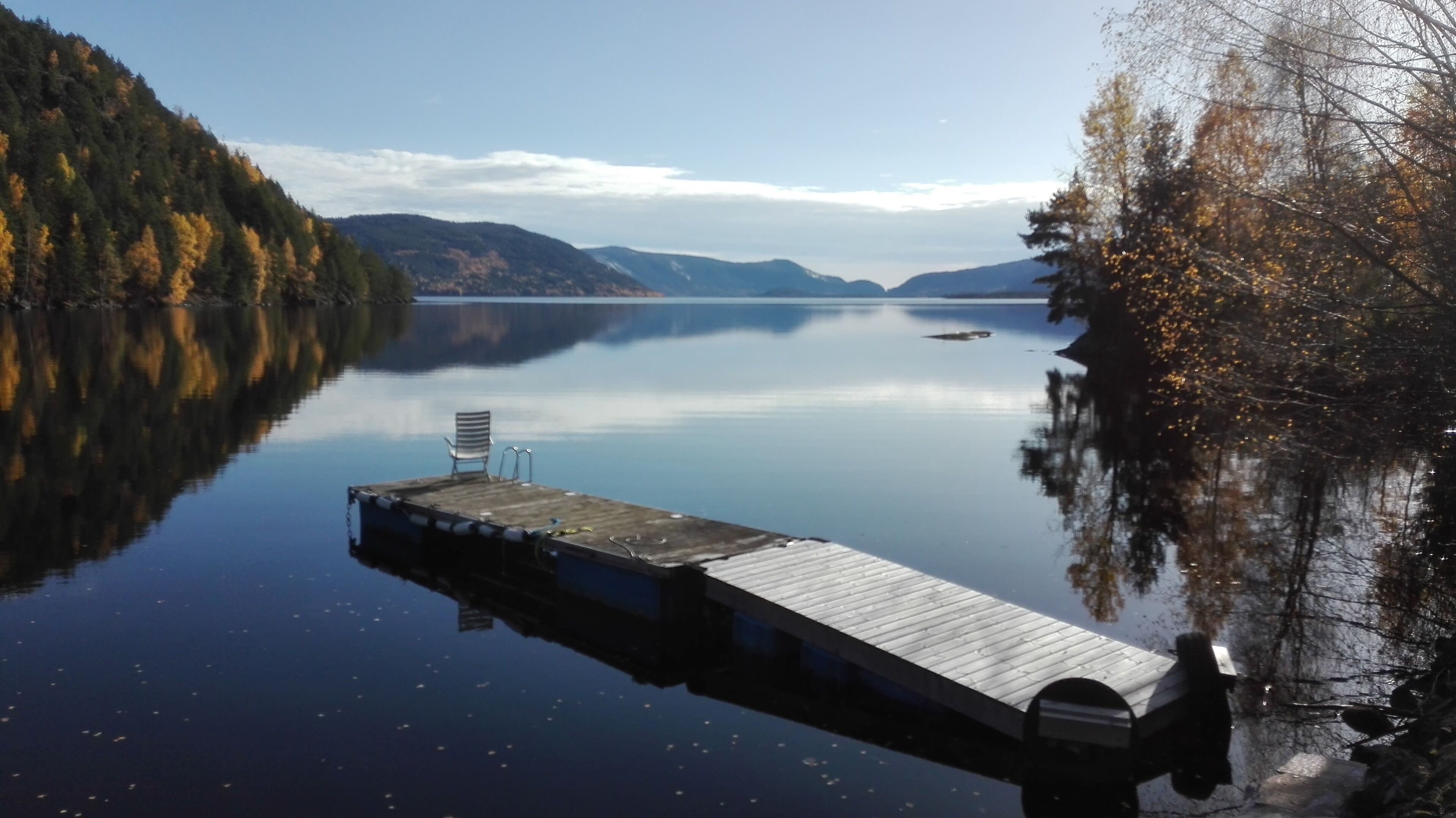 Een houten steiger die zich uitstrekt over kalm water, omringd door beboste heuvels.