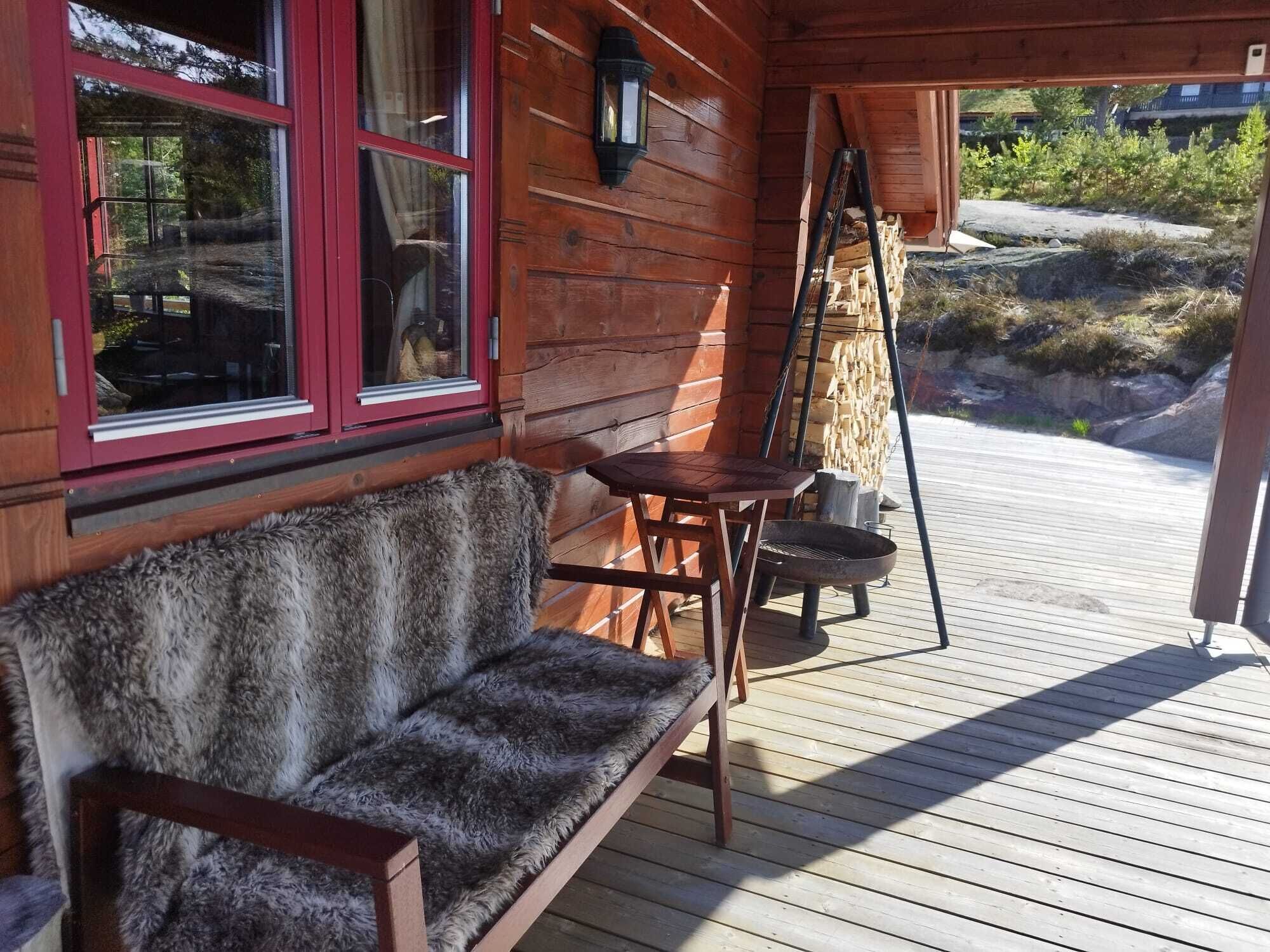 En træterrasse med bænk og bord, et vindue med rød ramme og en lygte.