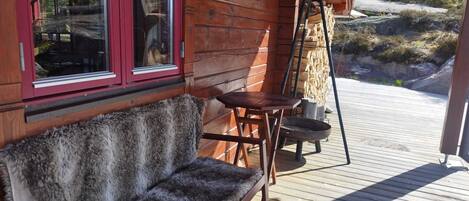 En træterrasse med bænk og bord, et vindue med rød ramme og en lygte.