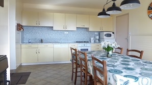 Una cocina con armarios de colores claros, salpicadero de azulejos, estufa, microondas y una mesa de comedor con sillas.