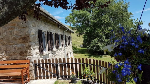 Un edificio de piedra con cerca de madera, un banco y un jardín con flores y un árbol.