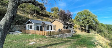 Una casa de piedra con valla de madera, un columpio y un patio cubierto de césped.