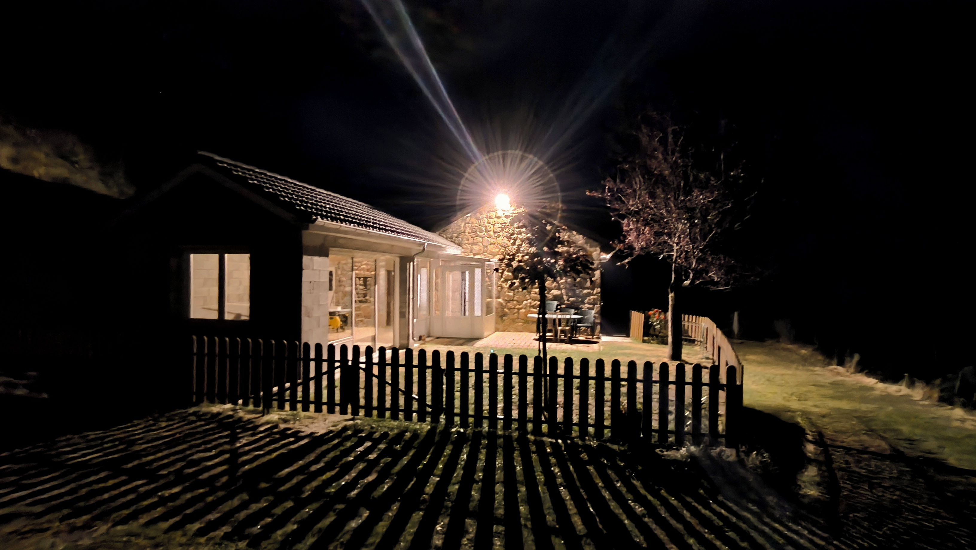 Ett hus med en mur av sten, ett staket av trä och en väl upplyst ytterdörr.