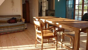 A cozy room with a wooden dining table and chairs, a striped sofa, and a view through large windows.