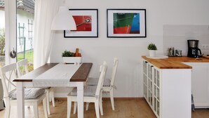 A modern kitchen with white cabinetry, a wooden countertop, and a dining area with white chairs and a checkered tablecloth.