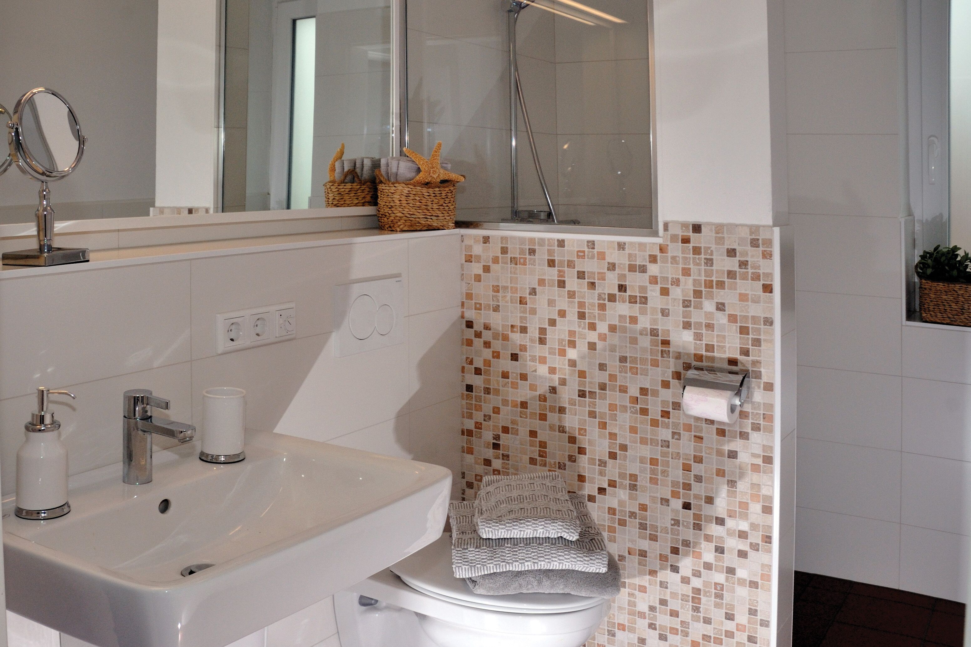 A bathroom with a white sink, a mirror, a toilet, and a shower.