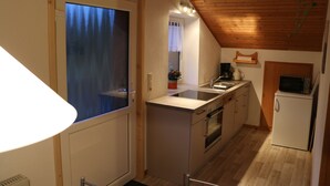 A compact kitchen with wooden ceiling beams, a refrigerator, a microwave, and a sink. - Country cottage with garden i (Sandbostel)