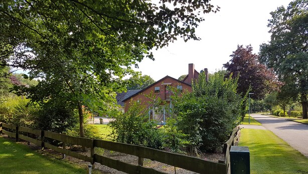 A residential area with a brick house, a wooden fence, and a well-maintained lawn. - Country cottage with garden i (Sandbostel)