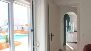 Habitación de hotel con puerta corrediza de vidrio que da a un área de piscina, una cama y un baño visible a través de un arco.