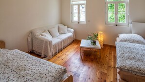 A cozy room with a sofa, two single beds, a small table with a plant, and two windows with views of greenery. - Idyllic, completely renovated half-timbered house in a listed courtyard (Neunkirchen-Seelscheid)