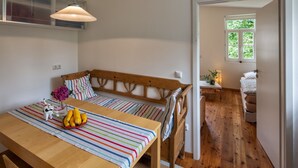 A cozy room with a wooden bed, a striped table, and a window with greenery outside. - Idyllic, completely renovated half-timbered house in a listed courtyard (Neunkirchen-Seelscheid)
