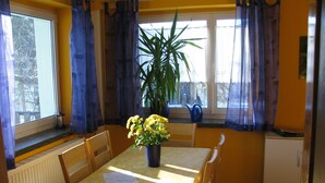 A dining area with a table set for four, a potted plant, and a window with curtains.