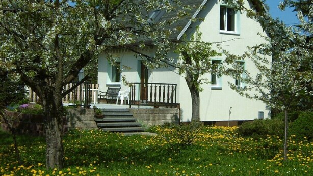 A house with a porch, steps leading up to the entrance, and a garden with yellow flowers.