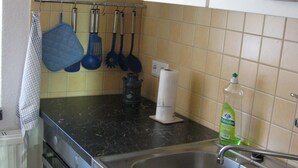 A kitchen with a microwave, stove, sink, and various utensils.