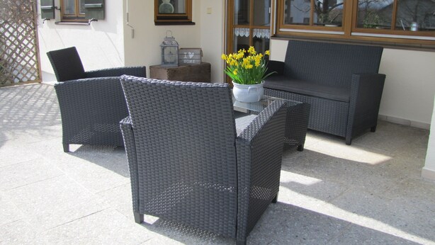 Eine Terrasse im Freien mit Korbmöbeln, einem Blumentopf und einem Schild mit der Aufschrift 'I love home'.