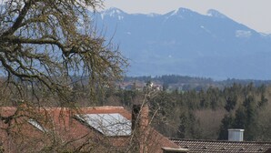 Eine Berglandschaft mit schneebedeckten Gipfeln im Hintergrund, ein Baum im Vordergrund und ein Gebäude mit rotem Ziegeldach.