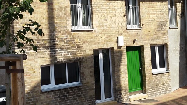 A two-story brick building with a green door, white-framed windows, and a satellite dish on the roof.