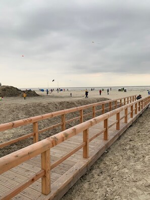 A wooden boardwalk leading to a sandy beach with a cloudy sky.