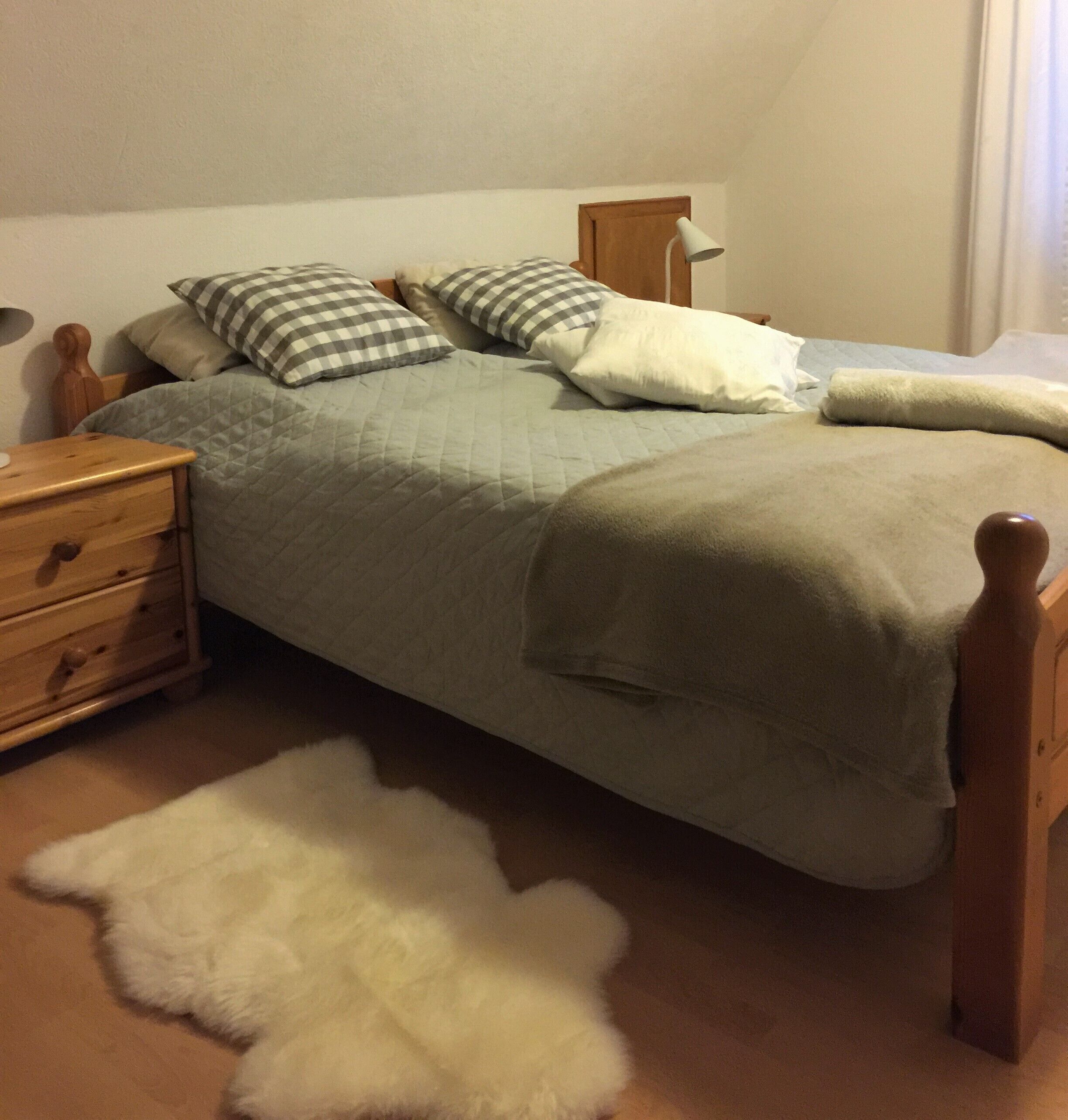 Uma cama com manta acolchoada, almofadas xadrez, cabeceira de madeira e mesa de cabeceira com gavetas.