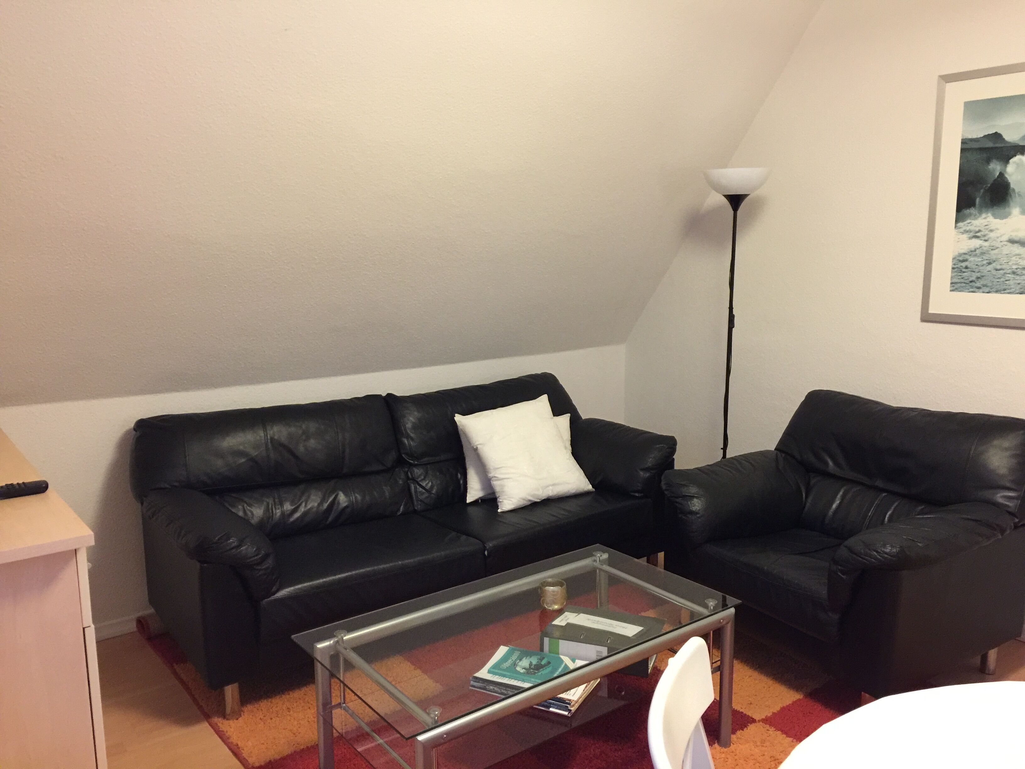 A living room with a black leather sofa, a glass coffee table, and a lamp.