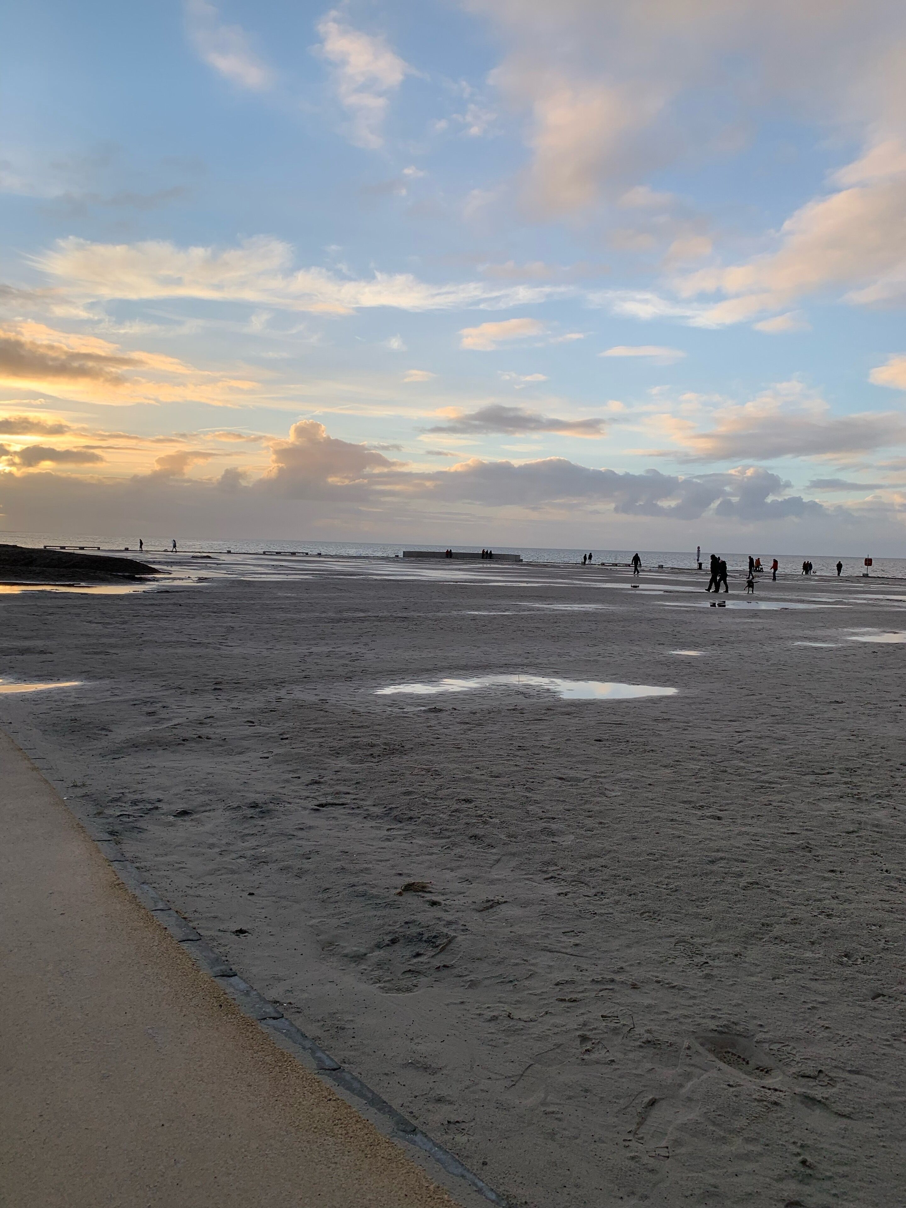 Ein Strand mit einer weiten Sandfläche und einigen Spaziergängern.