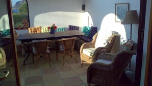Un patio soleado con una mesa de comedor rodeada de sillas de mimbre, un sofá y una lámpara.