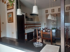 Une cuisine moderne avec des armoires blanches, un comptoir noir et des luminaires suspendus. On y trouve une table à manger avec des chaises et une plante en pot.