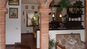 Une pièce avec des arches en briques, un canapé, un coin repas avec une table et une cuisine avec des étagères.