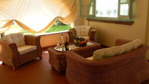 Une pièce chaleureuse, meublée de mobilier en osier, avec une fenêtre dont le volet est entrouvert et qui offre une vue sur la verdure environnante.
