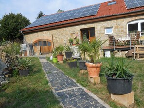 A stone house with a tiled roof, solar panels, and a paved pathway leading to the entrance.