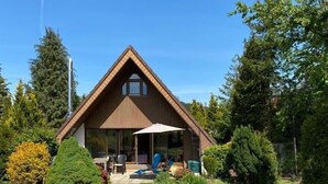 A wooden house with a triangular roof, a patio with outdoor furniture, and a well-maintained garden.