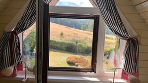 A room with a large window, curtains, and a view of a countryside landscape.