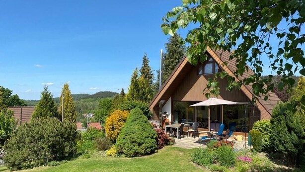 A house with a sloped roof, a patio with outdoor furniture, and a well-maintained garden.