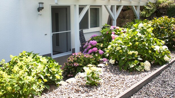A white building with a covered porch, a window, and a gravel pathway.