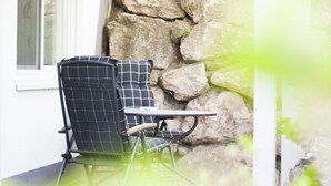 A chair with a checkered cushion and a small table, positioned against a stone wall.