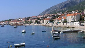 A coastal town with boats docked along the harbor, surrounded by residential buildings with red-tiled roofs. - The apartment is located on the first floor of our house, 50 meters from the sea (Bol)