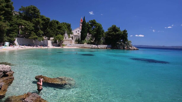 A coastal area with clear turquoise waters, rocky shorelines, and a historic building with a red roof. - The apartment is located on the first floor of our house, 50 meters from the sea (Bol)