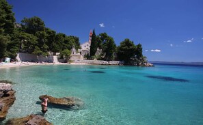 A coastal area with clear turquoise waters, rocky shorelines, and a historic building with a red roof. - The apartment is located on the first floor of our house, 50 meters from the sea (Bol)