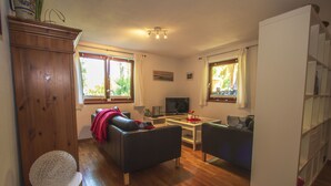 A living room with a sofa, a coffee table, a TV, and a bookshelf. - Lovingly furnished apartment in a Mediterranean style  (Dießen am Ammersee)