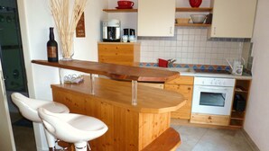 A kitchen with a wooden bar, white bar stools, a coffee maker, and a stove. - Lovingly furnished apartment in a Mediterranean style  (Dießen am Ammersee)