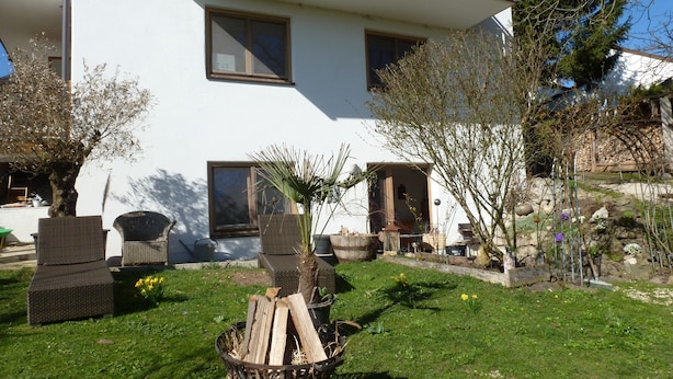 A white building with a balcony, a garden with chairs, and a fire pit. - Lovingly furnished apartment in a Mediterranean style  (Dießen am Ammersee)