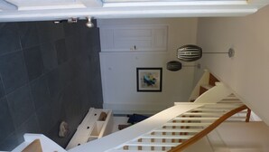 Una escalera con barandas blancas y peldaños de madera que lleva a una habitación con piso de baldosas oscuras.